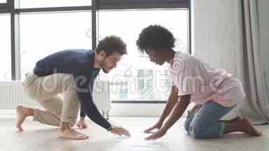年轻的多种族夫妇坐在地板上检查账单，学习文件，准备财务报告
